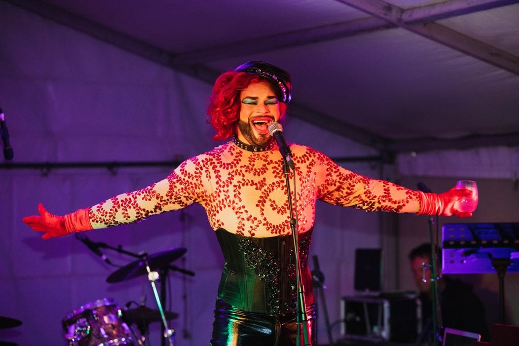 bearded man singing on stage with arms out